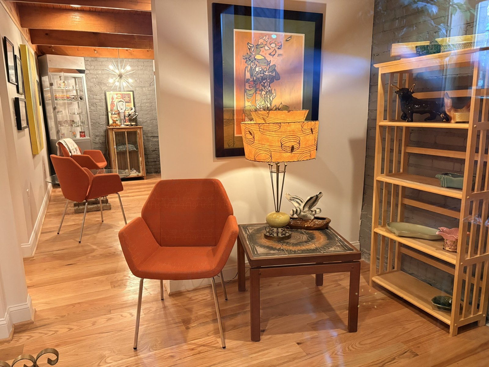 Burnt-orange mid-century lounge chairs beside a sculptural atomic-shade lamp and teak shelving in the shop